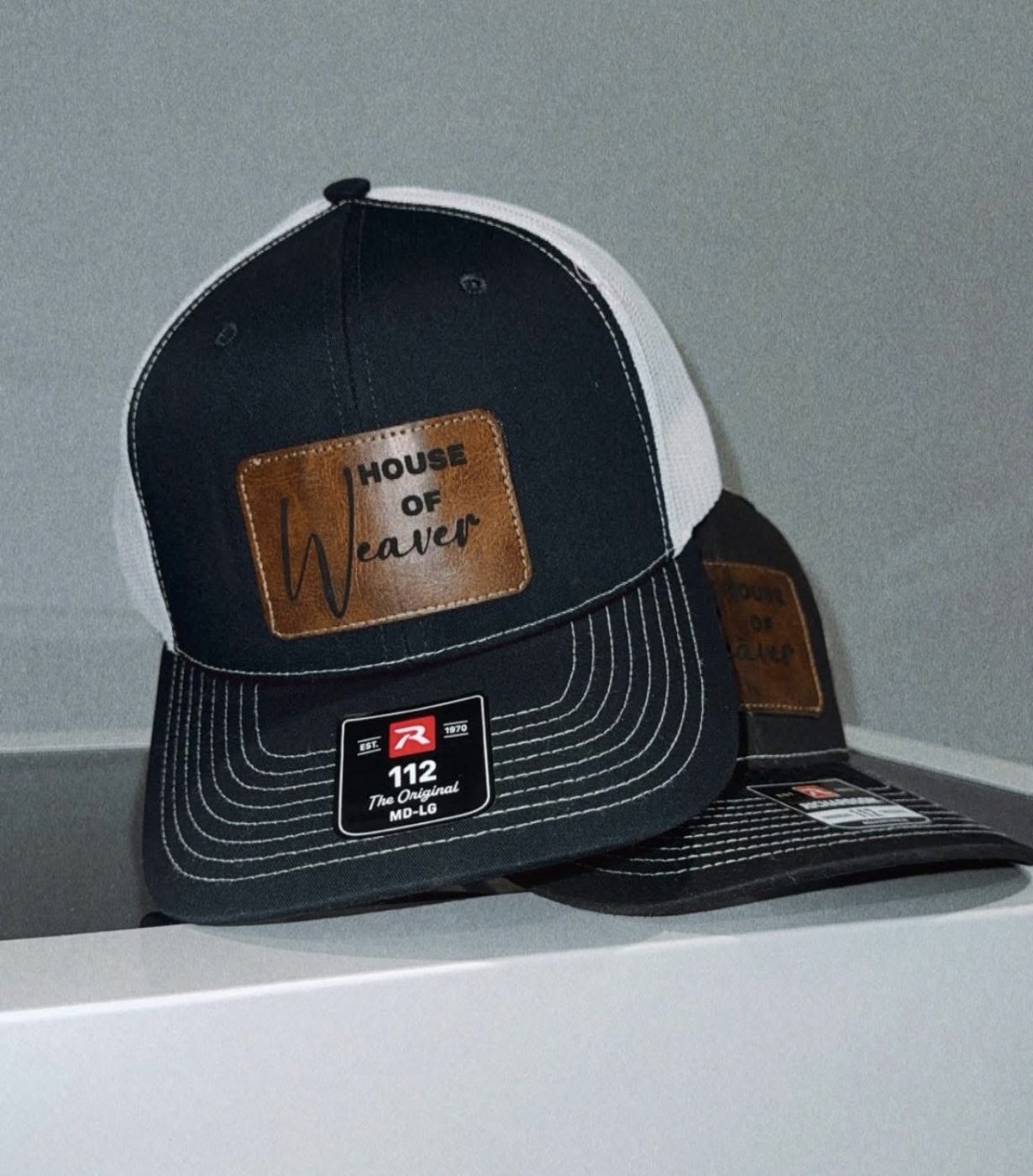 Navy and white trucker hat with a leather patch that reads House of Weaver